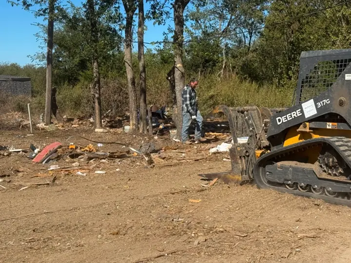 Skid steer clearing scattered debris from a rural lot